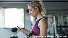 Sportliche junge Frau schaut auf ihr Smartphone und liest eine SMS beim Training | Verwendung weltweit
