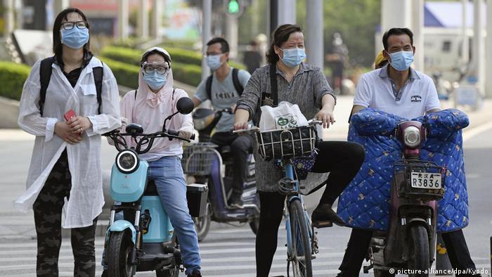 People wearing face masks and face shields ride motorcycles and bicycles
