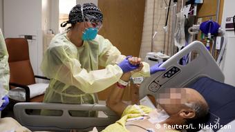 Врач в маске в больнице штата Калифорния стоит у постели в больным COVID-19