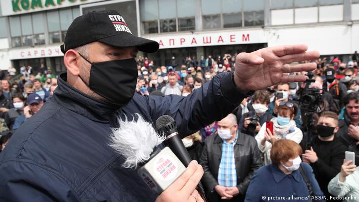 Siarhei Tsikhanouski, man with a face mask and a baseball cap pointing with his hand, a crowd behind him 