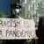 A protester in London holds a placard that says 'racism is a pandemic'