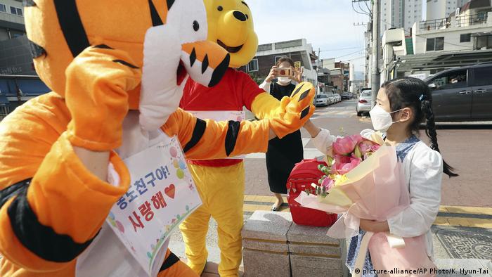 An elementary school student being welcomed by teachers in animal costumes in Daegu. An inordinate amount of pressure for implementation lies on the shoulders of teachers, who must join the students in using an online self-diagnostic system to record their own temperatures before classes. South Korea currently has under 12,000 confirmed cases.