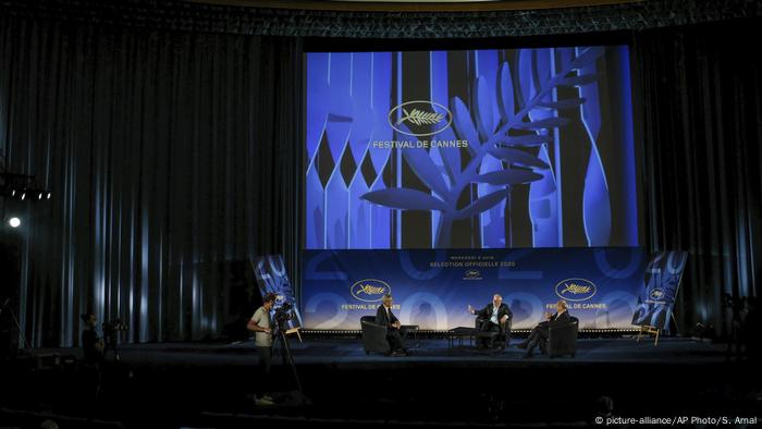 A discussion panel at the Cannes Festival sits on a dramatically lit stage. Behind the panel members is the logo of the Cannes Film Festival 2020.