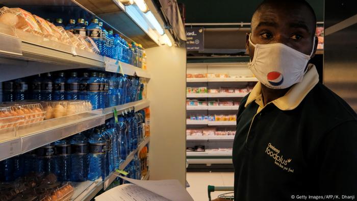 A man with a mask stands befores shelves at a supermarket