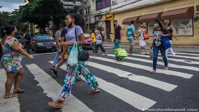 Pessoas de máscara com sacolas nas mãos atravessam rua do Rio de Janeiro