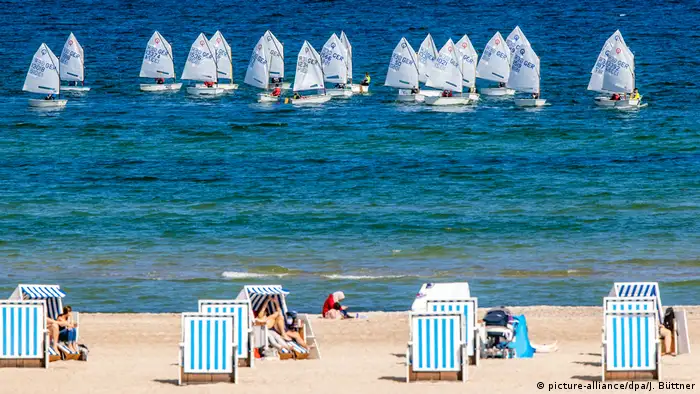 People sit in striped beach chairs along the coast.