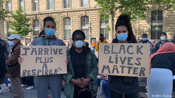 Protesters in Paris wearing face masks hold signs saying I can't breathe and Black Lives Matter