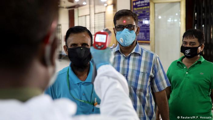 A security personnel checks the body temperature of customers with a thermal scanner at the entrance to a bank amid the coronavirus disease (COVID-19) outbreak in Dhaka