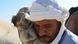A tour guide in the desert with his camel, which is pressing its face up against his A tour guide in the desert with his camel, which is pressing its face up against his