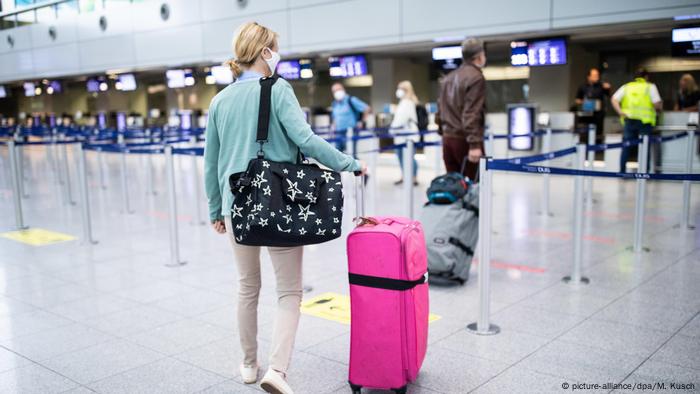 Germany, a woman with a large pink suitcase queuing for the check-in counter at Düsseldorf Airport