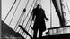Count Orlok stands on a ship's deck. He has bat-like ears, thick-eyebrows and long canines. Count Orlok stands on a ship's deck. He has bat-like ears, thick-eyebrows and long canines.