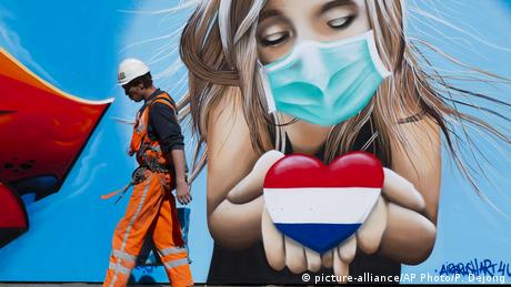 A large mural of a blonde girl wearing a mask and holding a heart-shaped Dutch flag. 