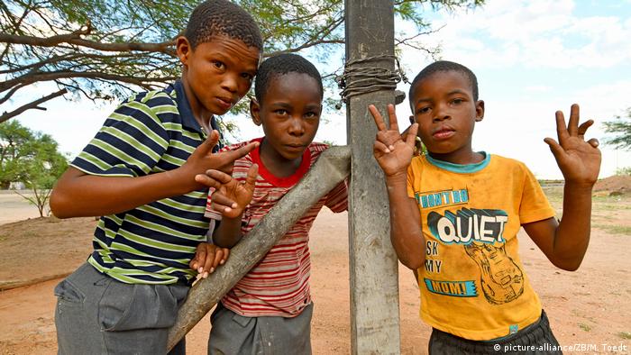 Three Nambian children pose by a fence post