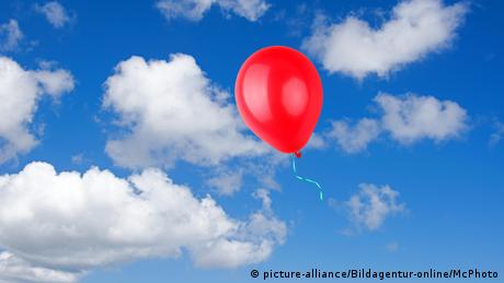 Roter Luftballon vor blauem Himmel mit Wolken