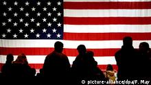 ARCHIV - 22.02.2005, Ramstein: Besucher stehen auf der Air Base in Ramstein vor einer US-Flagge im Gegenlicht. Mit der Großübung «Defender» wollen die USA im Frühjahr testen, ob eine Verlegung von Truppen in Europa reibungslos klappt. Foto: Frank May/dpa +++ dpa-Bildfunk +++ | Verwendung weltweit