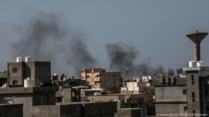 View of rooftops against a blurred sky, smoke rises