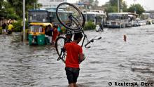 A man carries his bicycle as he crosses a flooded road after heavy rains in Ahmedabad, India, June 8, 2020. REUTERS/Amit Dave