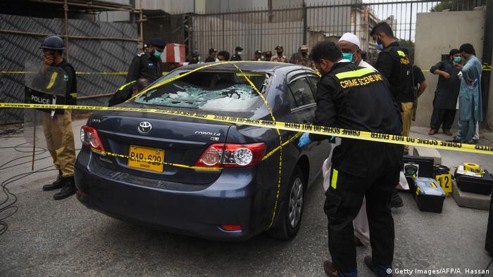 Policemen guard as members of Crime Scene Unit investigate around a car used by alleged gunmen at the main entrance of the Pakistan Stock Exchange building in Karachi