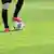 Pernas de jogador de futebol que mantém bola sob o pé num gramado