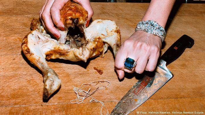 Helmut Newton - The Bad And The Beautiful | Hühnchen - Motiv mit gebratenem Hühnchen, einem großen Messe und einer schmuckbehängten Hand auf Holzbrett