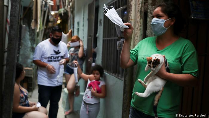A woman in a favela in Sao Paulo holds up a facemask