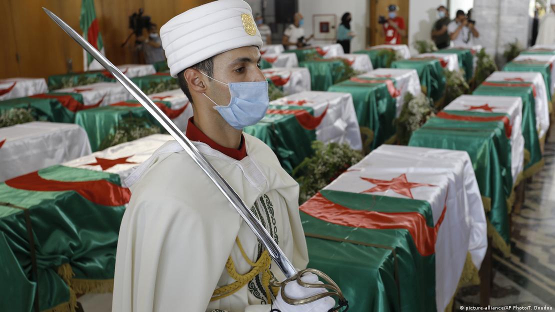 A man in front of several coffins covered in the Algerian flag