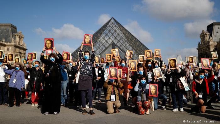 Mitarbeiter des Louvre stehen vor der Pyramide am Louvre und halten Bilder mit der Mona Lisa hoch 