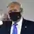 Donald Trump de terno, gravata azul e usando máscara preta.