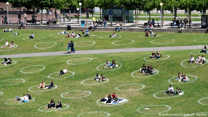 People sitting in circles marking correct distancing on a lawn on the banks of the river Rhine near Düsseldorf.