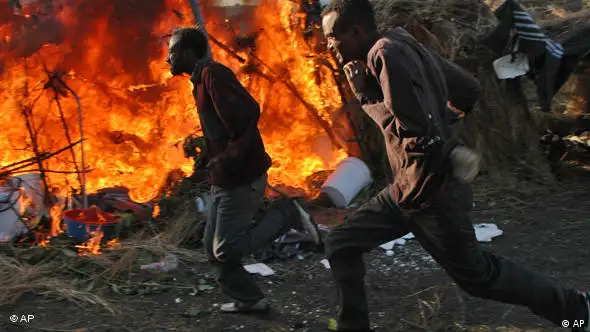Displaced Somalis run past a burning tent during the attacks against immigrants in South Africa in 2008.
