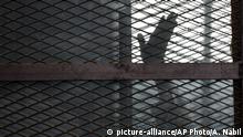 FILE - In this Aug. 22, 2015 file photo, a Muslim Brotherhood member waves his hand from a defendants cage in a courtroom in Torah prison, southern Cairo, Egypt. In some cells in Iran, Egypt, Syria and other countries in the Middle East, prisoners are crammed in by the dozens, with little access to hygiene or medical care. So if one infection gets in, the novel coronavirus could run rampant. (AP Photo/Amr Nabil, File) |
