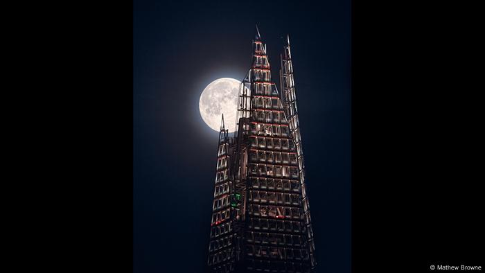 A full moon appears behind the slightly illuminated facade of a tall building (Photo: Mathew Browne).