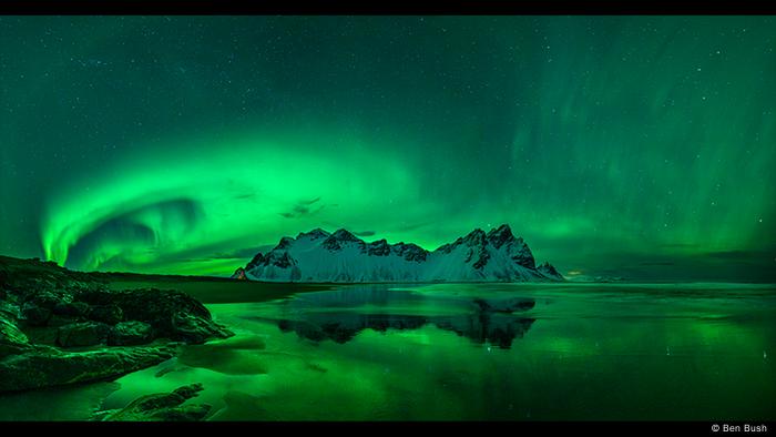 Night sky with water in the foreground, snow-capped mountains in the background, honeycomb neon-green Northern Lights in the sky (Photo: Ben Bush).