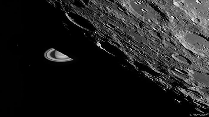 Schwarz-weiss Fotografie der Mondoberfläche mit diversen Kratern, dahinter taucht im Anschnitt der Planet Saturn mit Ringen auf (Foto: Andy Casely).