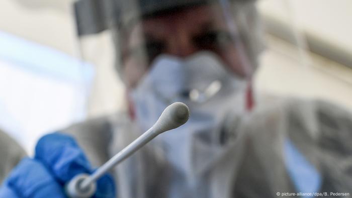 Someone in protective gear wields a testing swab