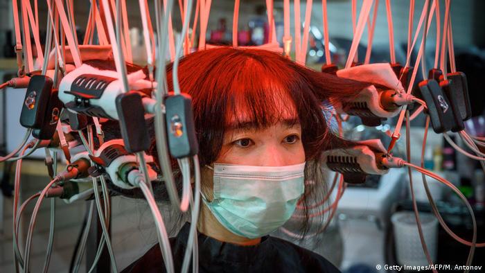 A woman wearing a face mask has her hair curled by a special equipment at a beauty salon in Bangkok on July 12, 2020