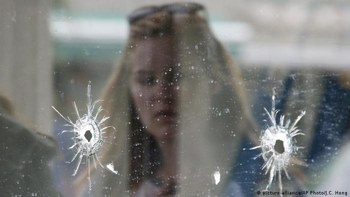 A woman looks at the bullet holes on the window 