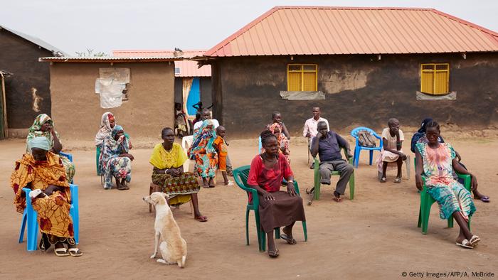 People sitting outside in an African village, listening to a presentation on coronavirus hygiene. 