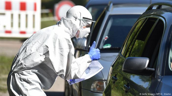 Mann in weißem Schutzanzug steht an der Drive-in-Teststation in der bayerischen Gemeinde Mamming neben einem Auto