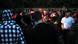 A large group of people holding glowsticks dance in a park A large group of people holding glowsticks dance in a park