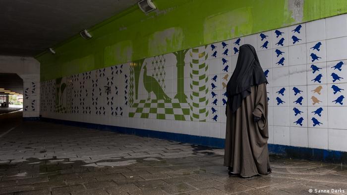 A woman stands under an empty tunnel wearing a black burqa