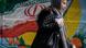 Iranians wearing face masks and single-use gloves walk past a mural displaying their national flag in Tehran Iranians wearing face masks and single-use gloves walk past a mural displaying their national flag in Tehran