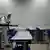 Sala de aula vazia. Uma pessoa com roupa de proteção branca e máscara anda pelo local com um aparelho pulverizador