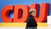 German Chancellor Angela Merkel walks past the party logo during a party convention of the Christian Democrats (CDU) in Karlsruhe, Germany, Monday, Dec. 14, 2015. (AP Photo/Michael Probst)