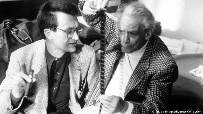 Wim Wenders und Sam Fuller in Anzügen im Gespräch am Film-Set, einer hält eine Filmspule in der Hand (Bild: imago images/Everett Collection)