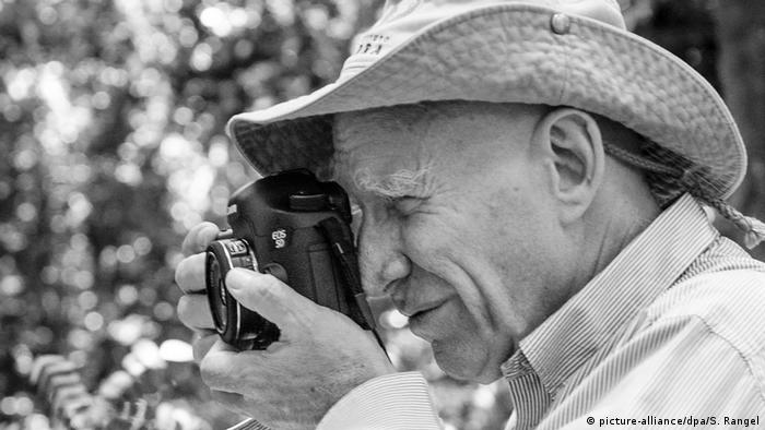 Sebastião Salgado, ein Fotograf mit Hut, nimmt ein Motiv mit seiner Kamera in den Blick, in Seitenansicht (Bild: picture-alliance/dpa/S. Rangel)