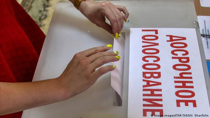 Женщина опубкает избирательный бюллетень в урну, на которой написано Досрочное голосование