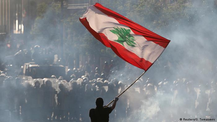 A demonstrator waves the Lebanese flag in front of riot police during a protest in Beirut, Lebanon