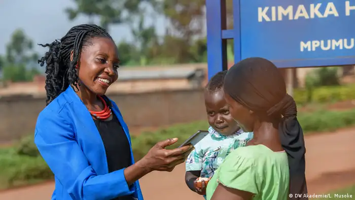 Female community reporter in Uganda interviewing a woman holding her baby 