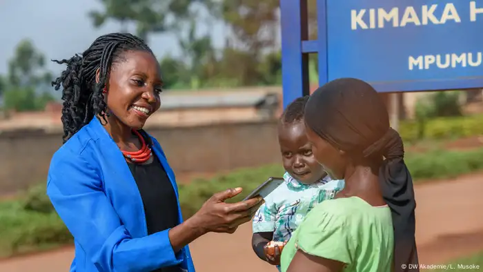 Female community reporter in Uganda interviewing a woman holding her baby 